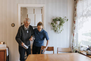 Female caregiver assisting senior man while walking at home - MASF37672