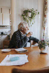 Senior man having tea while sitting at dining table in home - MASF37675