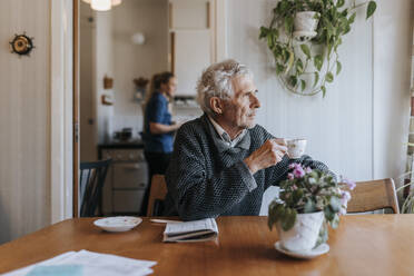 Thoughtful senior man holding tea cup while sitting at dining table in home - MASF37676