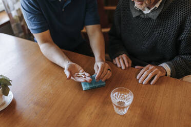 High angle view of female caregiver helping senior man while having medicines at home - MASF37677