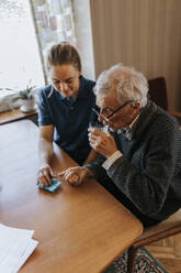 Hoher Blickwinkel eines älteren Mannes, der Medikamente einnimmt, während er mit einer Betreuerin zu Hause sitzt - MASF37680
