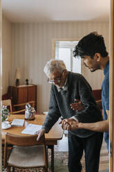 Männlicher Pflegehelfer hilft einem älteren Mann beim Gehen zu Hause - MASF37688