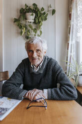 Smiling senior man sitting at dining table in home - MASF37695