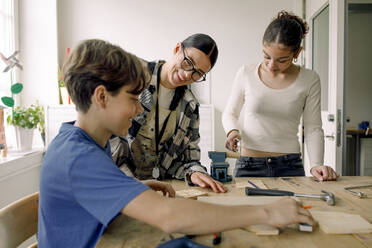 Smiling young teacher with male and female students during carpentry class - MASF37706