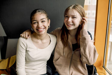Portrait of smiling teenage girl sitting with female friend at high school - MASF37727