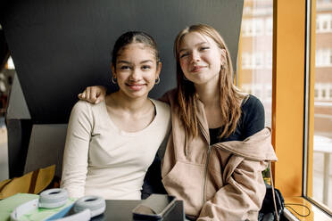 Portrait of smiling female teenage student sitting together at high school - MASF37728