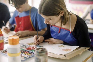 Female teenage student painting with brush during art class at high school - MASF37732