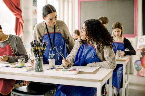 Lächelnde Lehrerin, die einem Teenager während des Kunstunterrichts an einer High School hilft - MASF37736