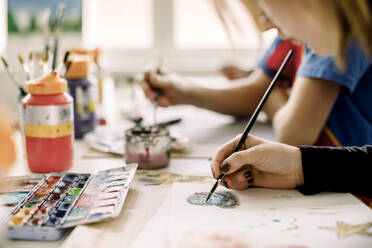 Hand eines weiblichen Teenagers, der während des Kunstunterrichts in der High School mit einem Pinsel auf Papier malt - MASF37739