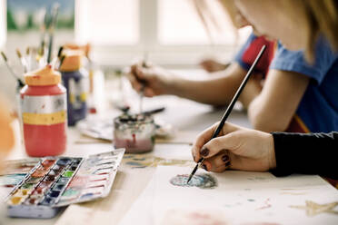 Hand of female teenage student painting on paper with brush during art class in high school - MASF37739