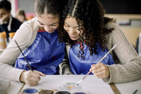 Lächelnde weibliche Teenager, die während des Malkurses in der High School Kunstwerke üben - MASF37741