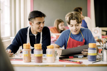 Lächelnder Teenager, der einem männlichen Freund während des Malkurses in der High School ein Kunstwerk zeigt - MASF37742