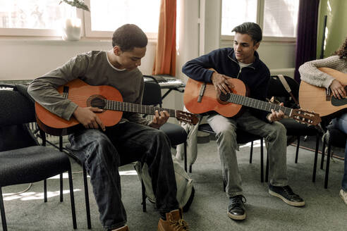 Teenager üben Gitarre auf einem Stuhl sitzend im Musikunterricht in der High School - MASF37753