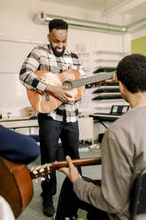 Männlicher Lehrer spielt Gitarre mit Schülern im Musikunterricht an einer High School - MASF37755
