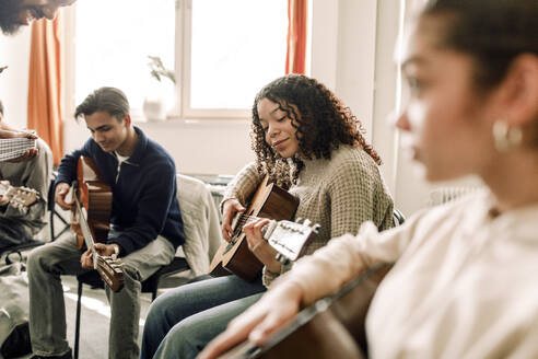 Lächelndes Teenager-Mädchen, das mit Freunden im Musikunterricht an der High School Gitarre übt - MASF37758