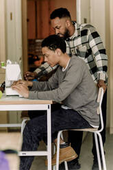 Jugendlicher, der im Kunstunterricht an der High School von einem Lehrer das Nähen mit der Nähmaschine lernt - MASF37761