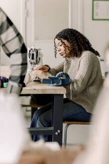 Teenage girl with curly hair using sewing machine in art class at high school - MASF37762