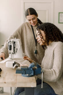 Lächelnde Lehrerin, die eine Schülerin bei der Arbeit an der Nähmaschine im Kunstunterricht der High School beobachtet - MASF37764