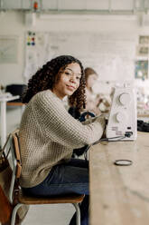 Seitenansicht Porträt einer weiblichen Teenager-Schülerin mit Nähmaschine auf dem Schreibtisch im Kunstunterricht in der High School - MASF37767