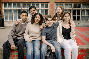 Lächelnde männliche und weibliche Teenager, die auf dem Campus einer High School zusammensitzen - MASF37779