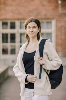 Porträt eines lächelnden weiblichen Teenager-Schülers mit Rucksack in der High School Campus stehen - MASF37780