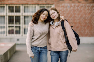 Portrait of smiling female students standing with arms around in high school campus - MASF37782