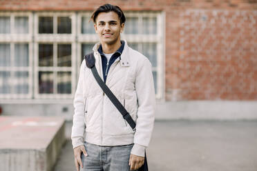 Portrait of smiling male teenage student with crossbody bag standing in high school campus - MASF37787