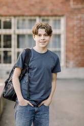 Porträt eines lächelnden männlichen Teenager-Schülers, der mit einem Rucksack auf einem Highschool-Campus steht - MASF37791