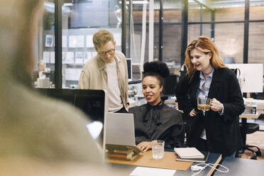 Smiling multiracial colleagues discussing over laptop while planning strategy at office - MASF37799