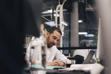 Businessman writing in diary at desk in office - MASF37802