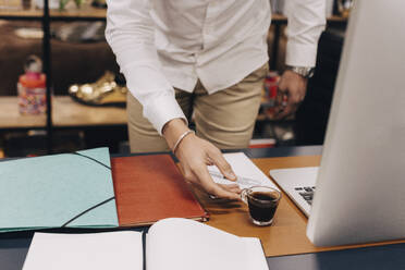 Midsection of businessman picking up coffee cup from desk in office - MASF37807