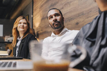 Businessman sitting with female colleagues at conference table in board room during meeting - MASF37820