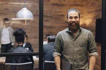 Portrait of smiling businessman with beard standing at doorway - MASF37838