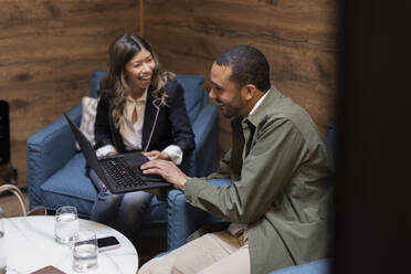 Cheerful business colleagues discussing over laptop while sitting in office - MASF37851