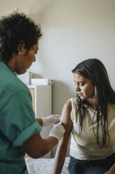 Mature doctor applying bandage on hand of young woman during vaccination in clinic - MASF37870