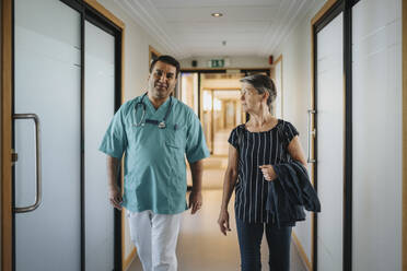 Doctor discussing with senior patient while walking in corridor of hospital - MASF37876