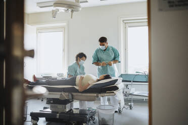 Male and female surgeons examining patient on bed in hospital - MASF37902