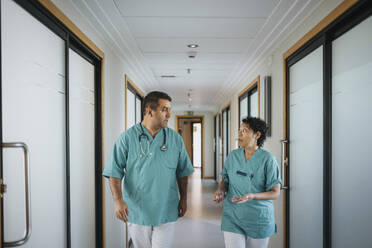 Multiracial male and female healthcare workers discussing while walking in corridor of hospital - MASF37920