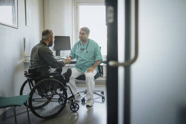Doctor discussing with male patient sitting in wheelchair at hospital - MASF37924