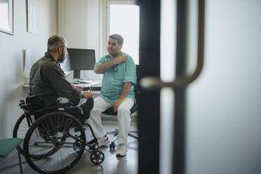 Doctor discussing with male patient sitting in wheelchair at clinic - MASF37925