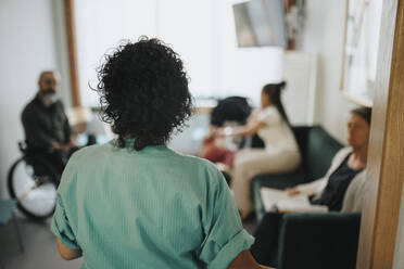 Rear view of nurse at doorway of waiting room in hospital - MASF37934