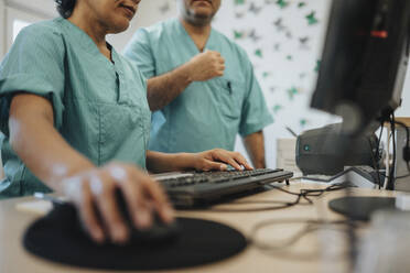 Midsection of nurse using computer by colleague at reception desk in hospital - MASF37942