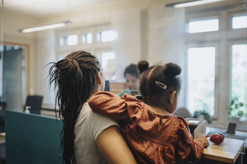 Mother carrying daughter while standing at reception desk in hospital - MASF37944