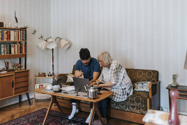 Ältere Frau, die einen Laptop benutzt, mit einem männlichen Pflegeassistenten, der zu Hause auf dem Sofa sitzt - MASF37949