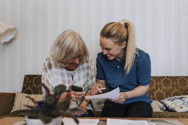 Glückliche Pflegerin, die einer älteren Frau, die zu Hause sitzt, medizinische Berichte erklärt - MASF37954