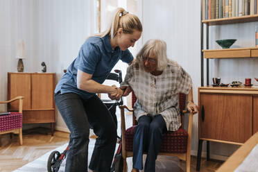 Weibliche Pflegekraft, die eine ältere Frau beim Sitzen auf einem Stuhl zu Hause unterstützt - MASF37958