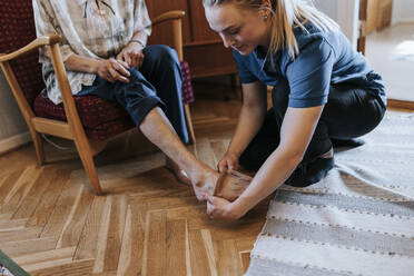 Weibliche Pflegekraft hilft einer älteren Frau, zu Hause Socken zu tragen - MASF37959