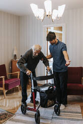 Männliche Pflegekraft, die einen älteren Mann bei der Benutzung einer Gehhilfe zu Hause unterstützt - MASF37976
