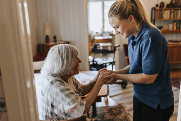 Lächelnde Mitarbeiterin im Gesundheitswesen hält die Hände einer älteren Frau zu Hause - MASF37985