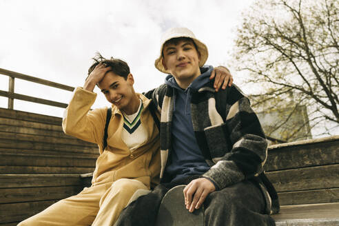 Portrait of smiling male friends sitting together on steps - MASF38009